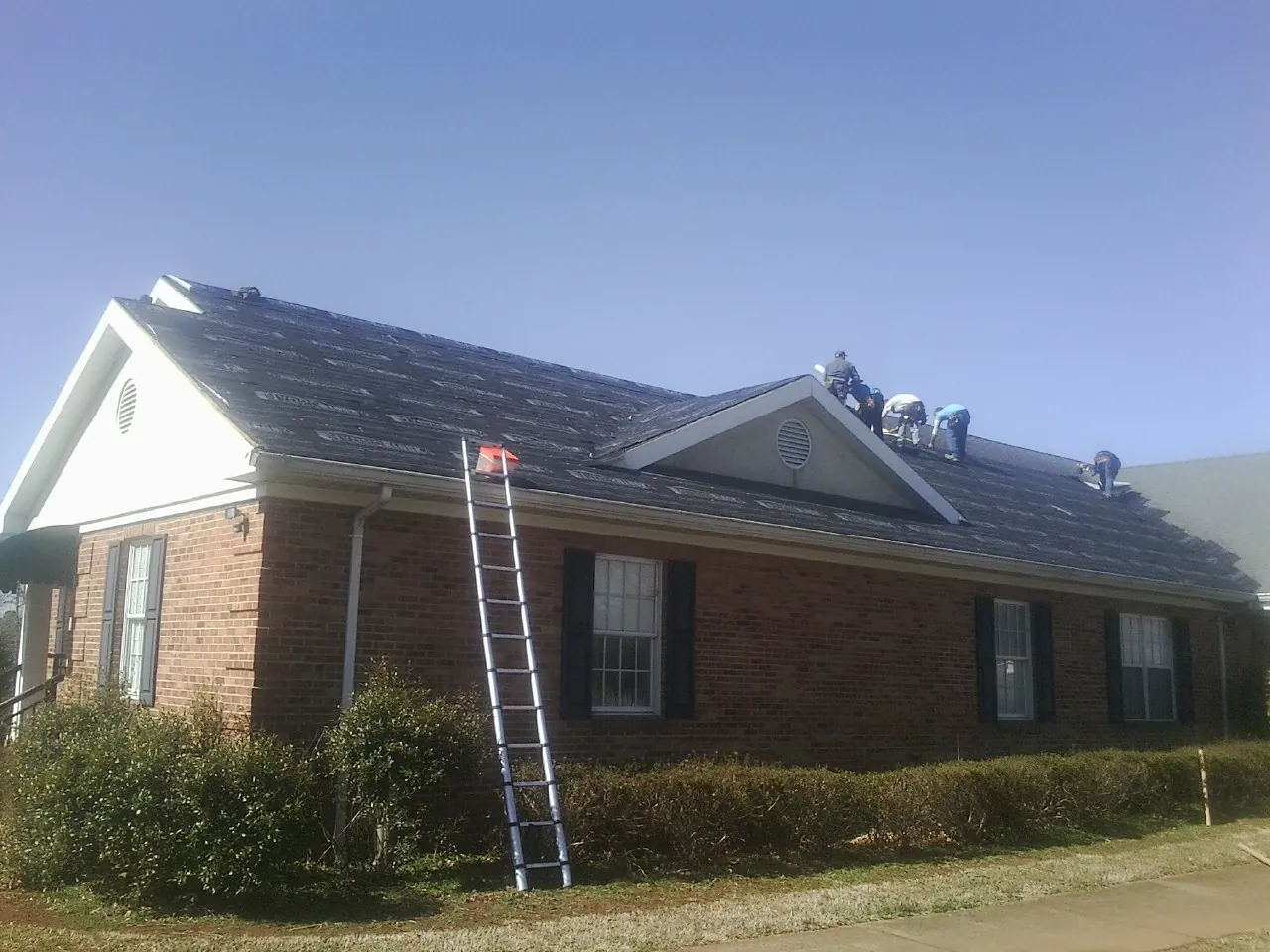 Crew tearing shingles off a brick ranch roof with a ladder set — Metal Roof Repair work by our crew in Bunkerville