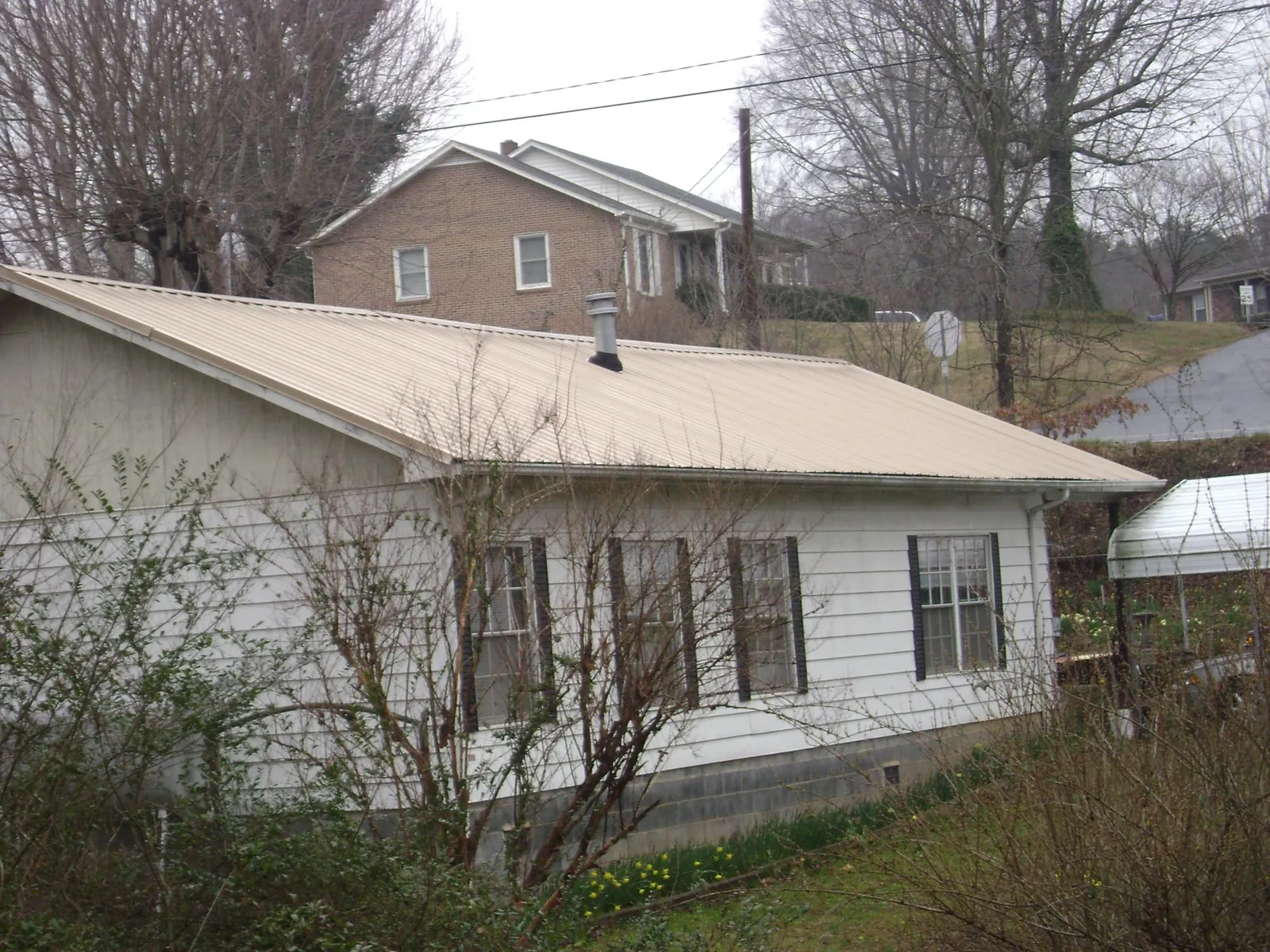 Tan metal roof on a white sided house set into a hillside — Commercial Roofing by Roofing Brothers in Bunkerville